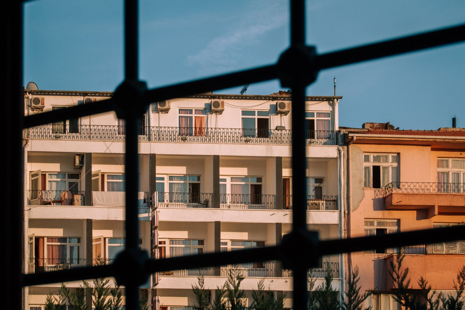 View of multi-story residential buildings through bars, showcasing urban architecture in warm daylight.